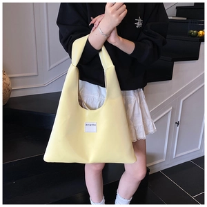 Detail view of the yellow velvet tote bag featuring a unique knotted handle and brand patch