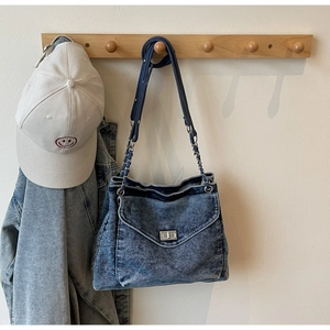 Close-up of washed blue denim shoulder bag with silver chain strap and twist lock detail