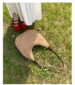 Chic woven crescent shoulder bag with brown leather strap on a lush green lawn