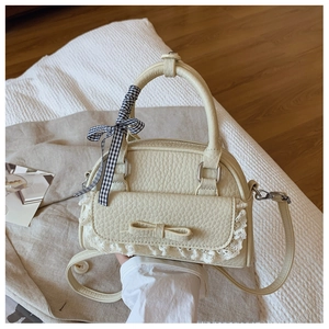 Detailed view of cream-colored shell bag with lace trim and leather bow decoration