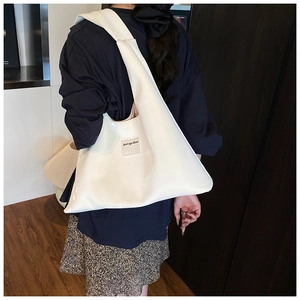 Detail of white glossy PU leather tote bag showing wide shoulder strap and brand patch