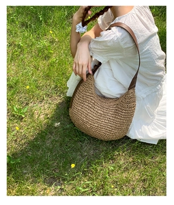 Detail of hand-woven straw crescent bag with brown leather strap on green grass
