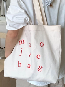 Large white canvas tote bag with red lettering shown on a model's shoulder for casual use