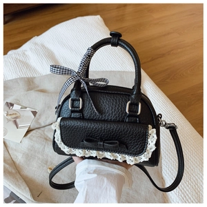 Detail of black lychee grain shell bag featuring lace trim and a plaid ribbon bow