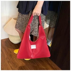 Detail of red glossy tote bag with minimalist logo tag and spacious hobo design