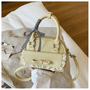 Detail of light yellow shell bag with lace edges, bow pocket, and ribbon handle
