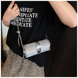 Detail of silver cylinder bag with wavy texture and gold M-logo buckle on leather