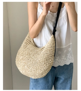 Detail view of woven straw shoulder bag with black leather strap and textured hobo design
