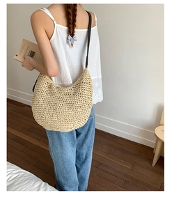 Detail of a large beige woven straw shoulder bag with black strap on a model
