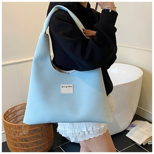 Detail of light blue velvet hobo bag with wide strap and branding label on front