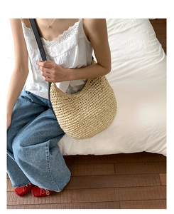 Close-up of beige woven hobo bag with black leather strap on a minimalist background