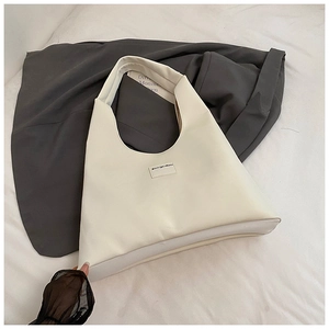 Detail view of a minimalist cream white faux leather tote bag with small square patch