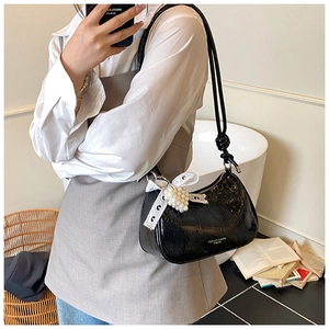 Detail of black patent leather hobo bag with pearl charm and lace bow decoration