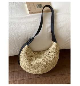 Close-up of beige woven straw shoulder bag with black leather strap and gold buckle