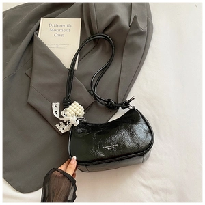 Detail of black glossy cloud bag with elegant pearl lace pendant on grey fabric