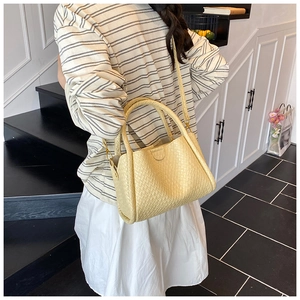 Détail de la texture tressée et des ferrures dorées d'un sac seau jaune crème femme