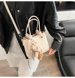 Detail of off-white lychee texture bucket bag with knotted handles and plush bear charm