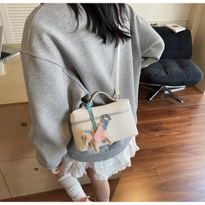 Dettaglio macro della borsa beige in pelle martellata con ciondolo pegaso rosa