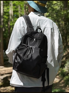 Rear view of a black waterproof nylon backpack worn outdoors in a lush forest setting