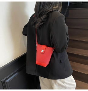 Detail shot of a red bucket bag with litchi grain texture and silver metal lock on a model