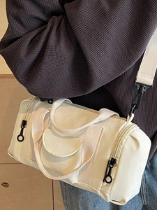 Minimalist cream cylinder boston bag with black zippers and adjustable shoulder strap