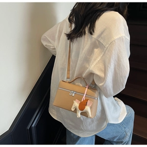Dettaglio borsa in pelle color cammello con ciondolo a cavallo indossata da modella