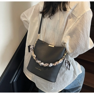 Detail of black pebbled leather bucket bag with silk scarf on gold chain handle
