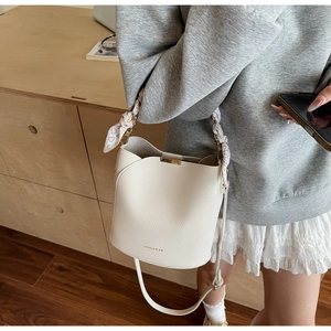 Close-up of cream bucket bag with lychee texture, silk scarf handle and gold hardware