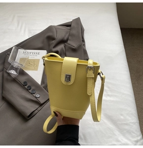Detailed view of yellow lychee leather bucket bag with silver buckle on art books