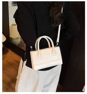 Detail of white leather handbag with dual cylindrical handles and embossed logo
