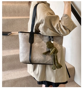 Gray tote bag detail with black trim and a cute green frog plush charm on the shoulder strap