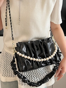 Sac nuage plissé noir chic avec poignée en perles et fini brillant porté par un mannequin