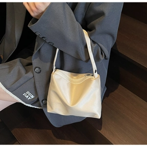 Sac à bandoulière minimaliste en satin beige au design trapèze porté par un mannequin