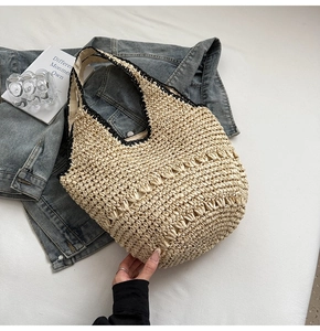 Detailed close-up of woven straw tote bag featuring black trim and contrast stitching