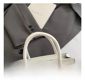 Detailed view of the round tubular handle and smooth metal zipper on the white handbag
