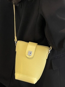 Minimalist yellow leather bucket bag with silver clasp shown on a dark suit