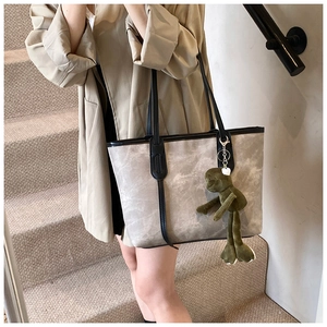 Detail view of large grey marble tote bag with black straps and a green frog plush charm