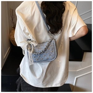 Détail du sac à bandoulière en denim bleu clair avec clous en strass et breloque perle