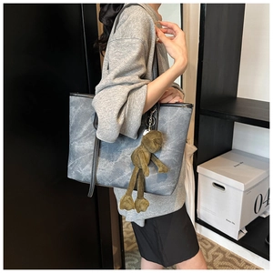 Detail of large tote bag with grey stone texture, black straps and green frog pendant
