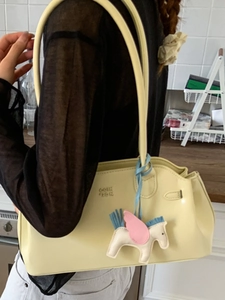 Sac bandoulière en cuir jaune pâle avec breloque pégase colorée porté à l'épaule