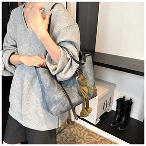 Detailed view of grey marble pattern tote bag with green plush frog charm on shoulder