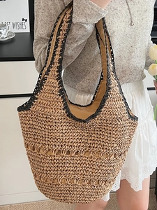 Hollow beige woven tote bag with black trim carried by a model for a beach vacation look