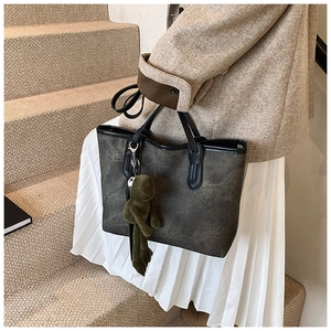 Detail of dark grey tote bag with vintage matte texture and green plush frog charm decoration