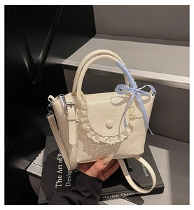 Detailed macro view of beige leather handbag with lace trim and blue checkered bow