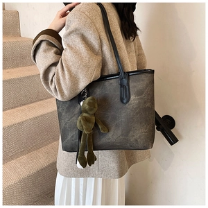 Detail shot of a dark grey tote bag with vintage texture and a green frog plush charm