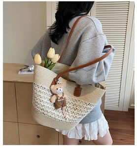 Detail of large woven straw shoulder bag with leather strap and cute bear charm
