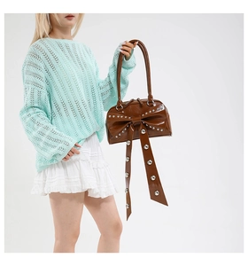 Detail showing the brown glossy leather shoulder bag with a large bow and silver rivets