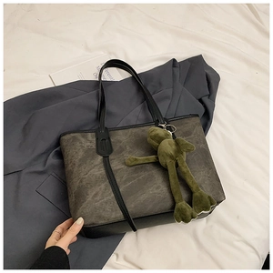 Flat lay of a large dark grey marble print tote bag with a green frog plush charm accessory
