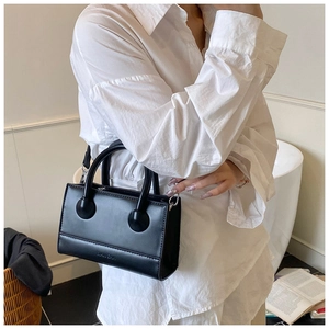 Detail of minimalist black leather handbag with round handle hardware and logo embossing