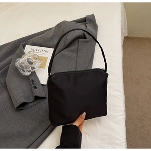Détail du sac bandoulière minimaliste en nylon noir avec fermeture éclair sur lit blanc